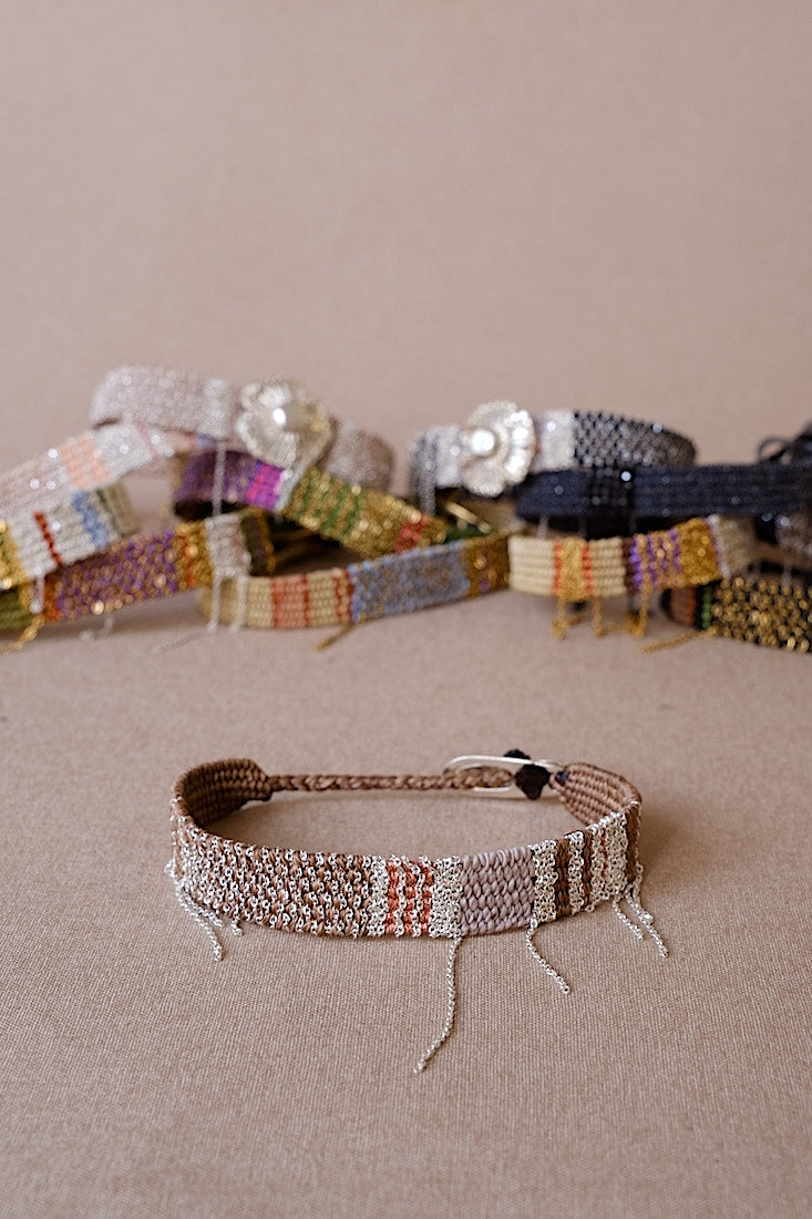 Close-up of a woven bracelet with other bracelets in the background on a beige surface.