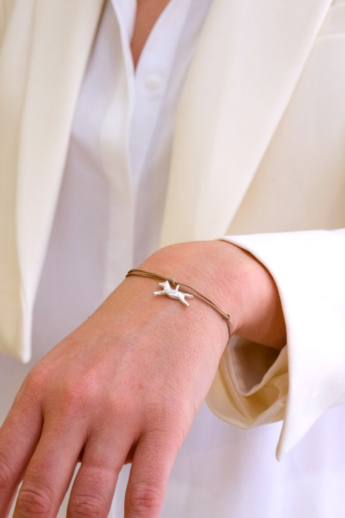 Hand wearing a delicate bracelet with a small foal charm against a white background