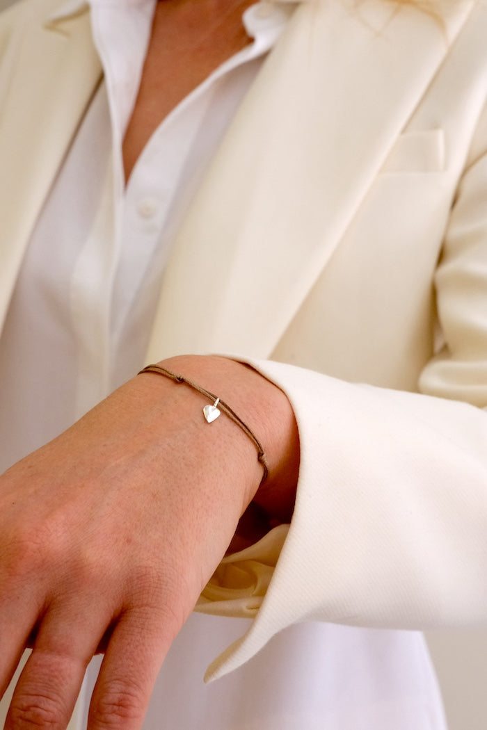 Close-up of a person wearing a thread bracelet with a heart charm.  Katia Alpha jewelry, Barcelona.