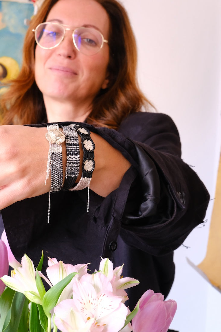 Woman wearing multiple bracelets and a black outfit with flowers in the foreground. Hand made bracelet, Barcelona studio, Kata Alpha Art.
